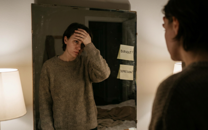 Pessoa pensativa em frente ao espelho com expressao de cansaco emocional, duvida entre burnout e depressao